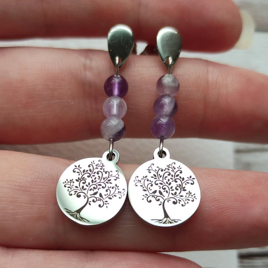 Boucles d'oreilles Arbre de Vie en acier inoxydable argenté tenues délicatement dans la main.