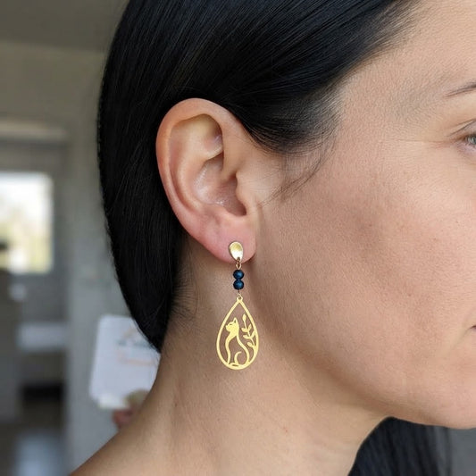 Boucles d'oreilles chat et feuillage ajouré en laiton et œil de faucon portées, mettant en valeur leur élégance et leur éclat doré.