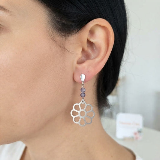 Boucles d'oreilles fleur ajourée en acier inoxydable et améthyste portées, mettant en valeur leur élégance et leur éclat argenté.