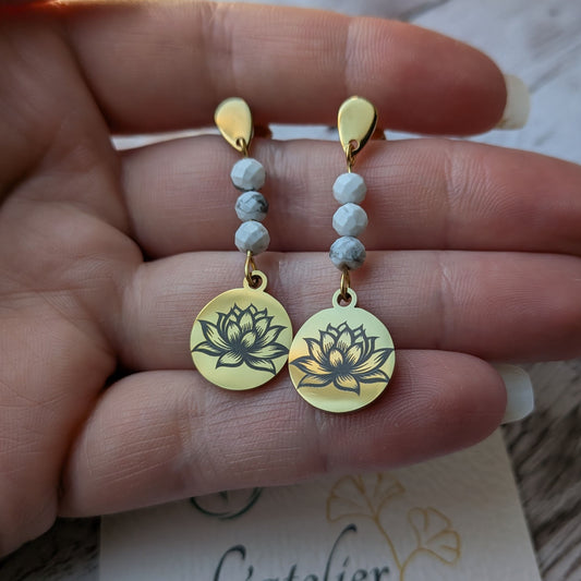 Paire de boucles d'oreilles fleur de lotus dorées avec howlite, tenues délicatement à la main.