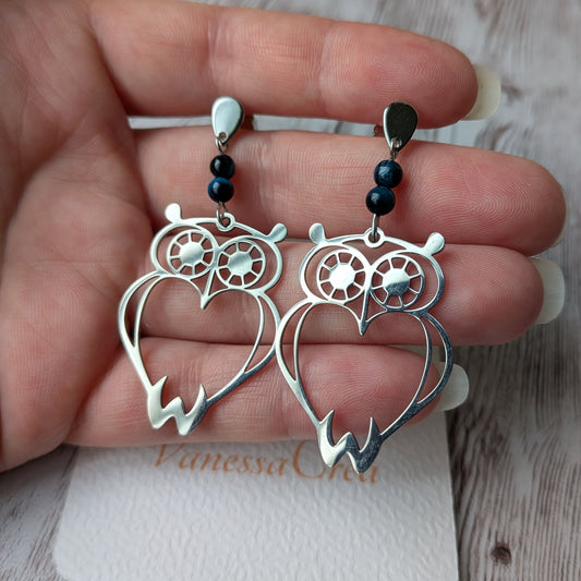 Paire de boucles d'oreilles hibou argenté en acier inoxydable tenue en main.