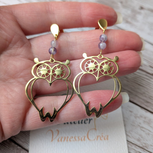 Paire de boucles d'oreilles hibou dorées en acier inoxydable tenue en main.