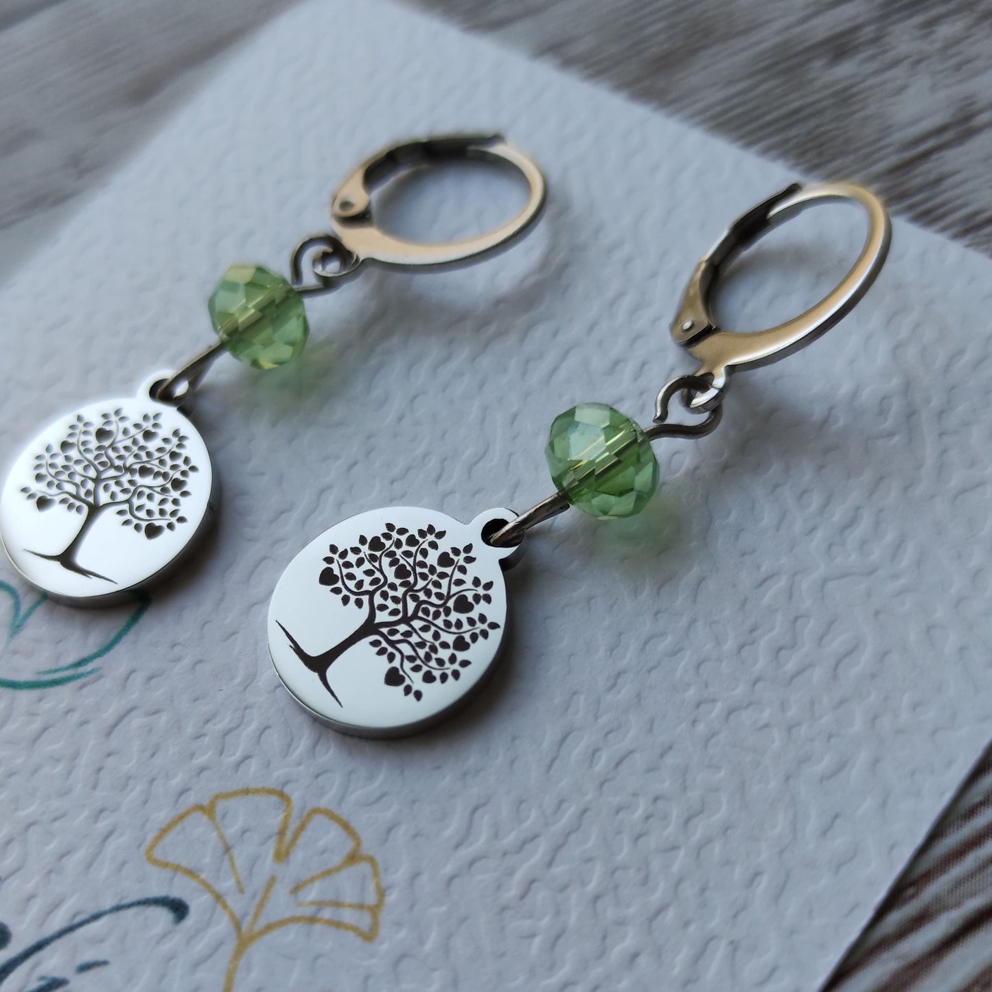 Boucles d'oreilles avec fermoir levier français, cristal à facettes et médaillon rond en acier inoxydable gravé d'un arbre de vie avec cœurs.