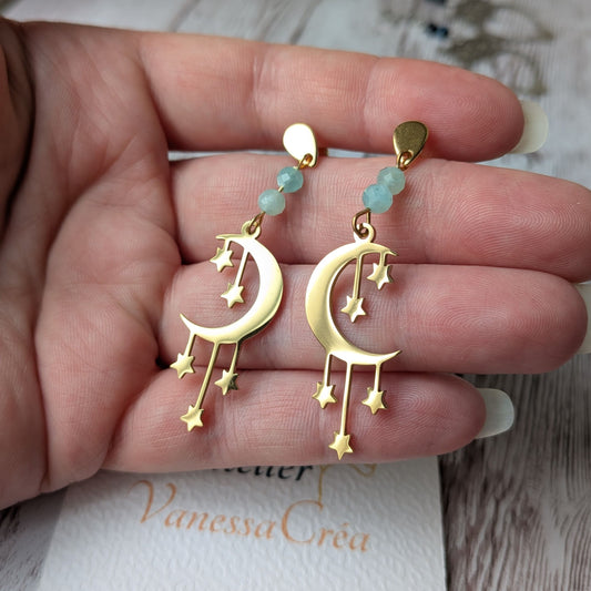 Paire de boucles d'oreilles lune et étoiles dorées en acier inoxydable tenue en main.