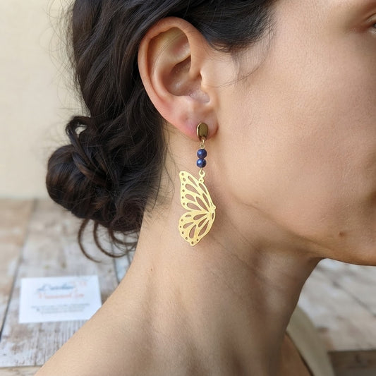 Boucles d'oreilles papillon ajouré en laiton et améthyste portées, mettant en valeur leur finesse et leur légèreté.