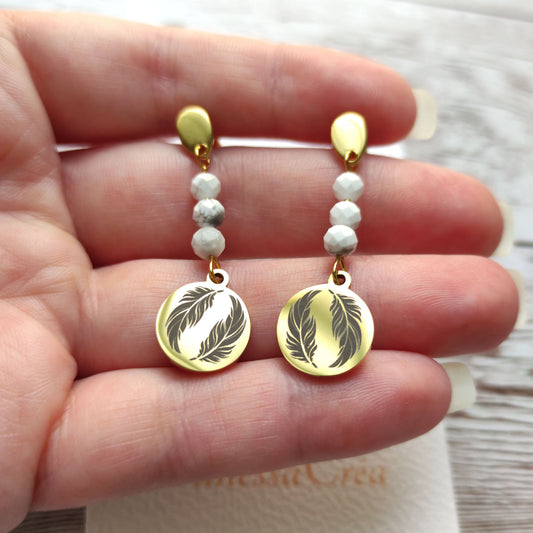 Boucles d'oreilles plume dorées en acier inoxydable tenues délicatement dans la main.