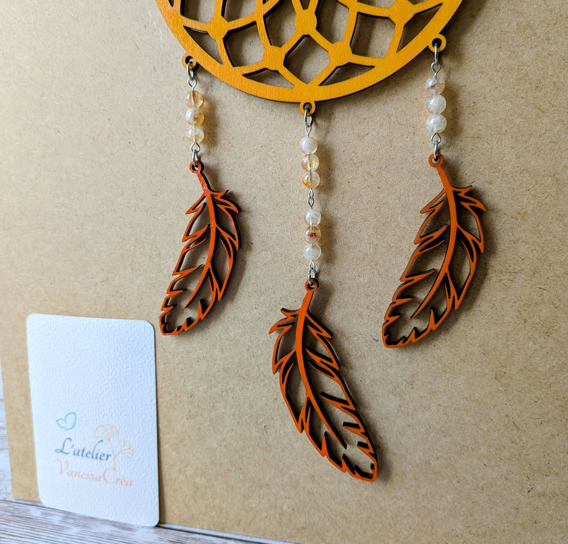 Attrape-rêve artisanal en bois de tilleul jaune safran zoom sur les plumes découpées et perles de citrine.