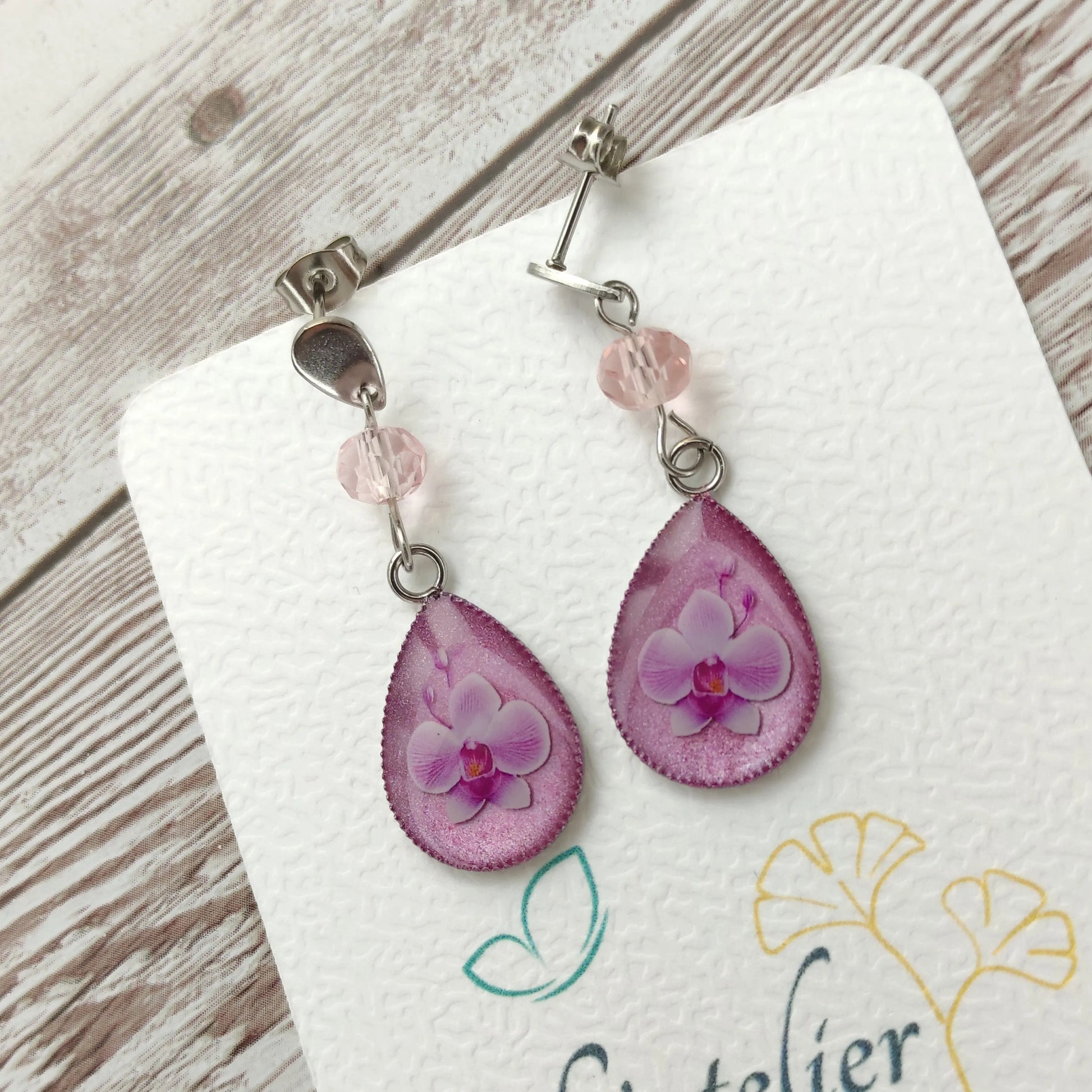 Boucles d'oreilles goutte en résine avec véritable orchidée rose pastel et clou en acier inoxydable argenté.