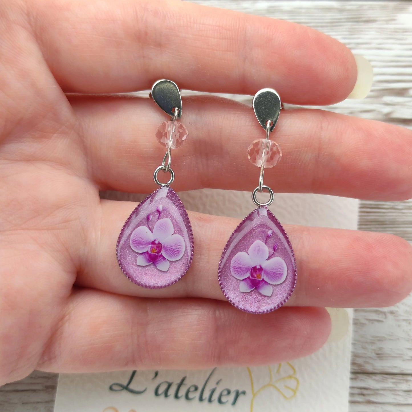 Détail d'une boucle d'oreille fleur orchidée résine nacrée avec cristal étincelant et finitions argentées.