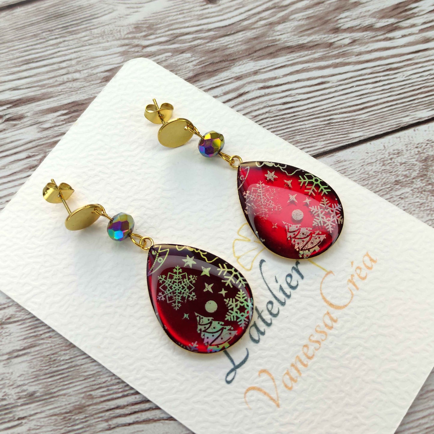 Boucles d'oreilles goutte Noël rubis en résine avec inclusions holographiques de sapins et flocons.