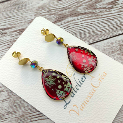 Boucles d'oreilles goutte Noël rubis en résine avec inclusions holographiques de sapins et flocons.
