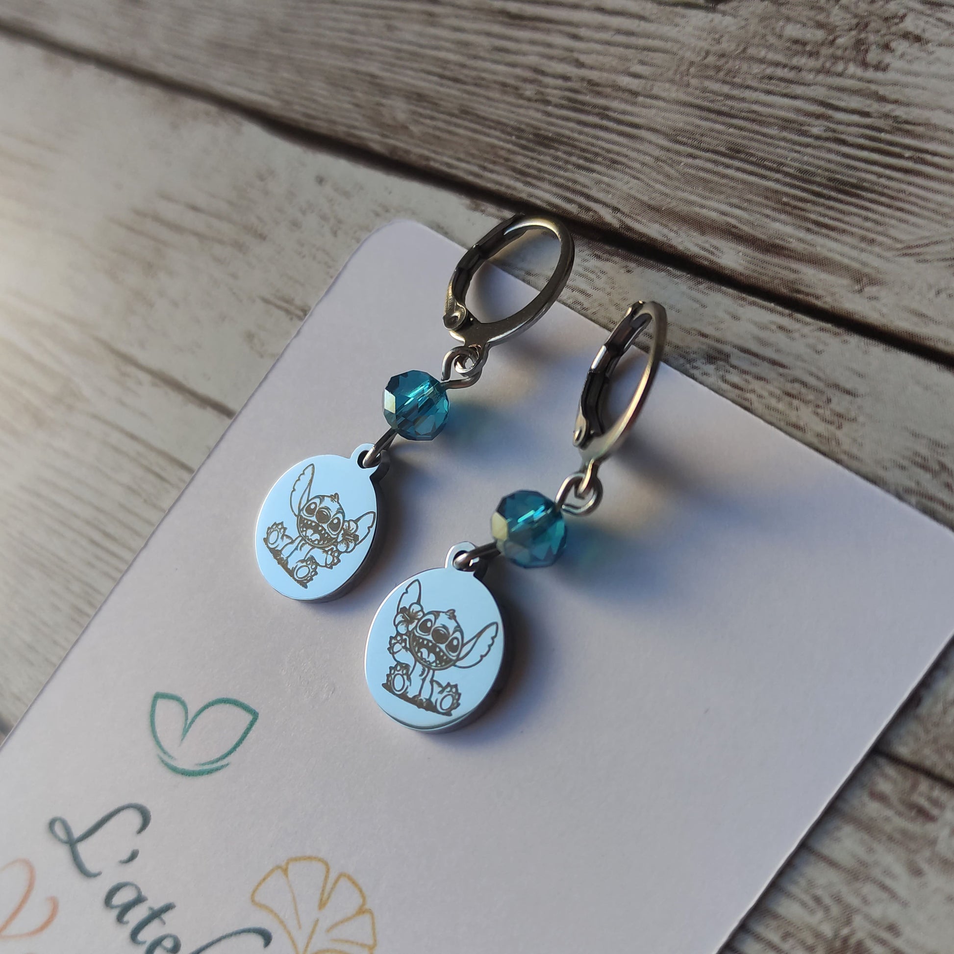 Boucles d'oreilles pendantes en acier inoxydable avec gravure laser de Stitch et une fleur, surmontées d'un cristal bleu