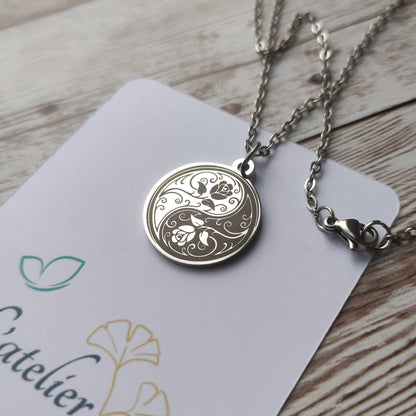 Collier médaille ronde en acier poli miroir avec gravure laser d'un symbole Yin Yang entrelacé de roses.