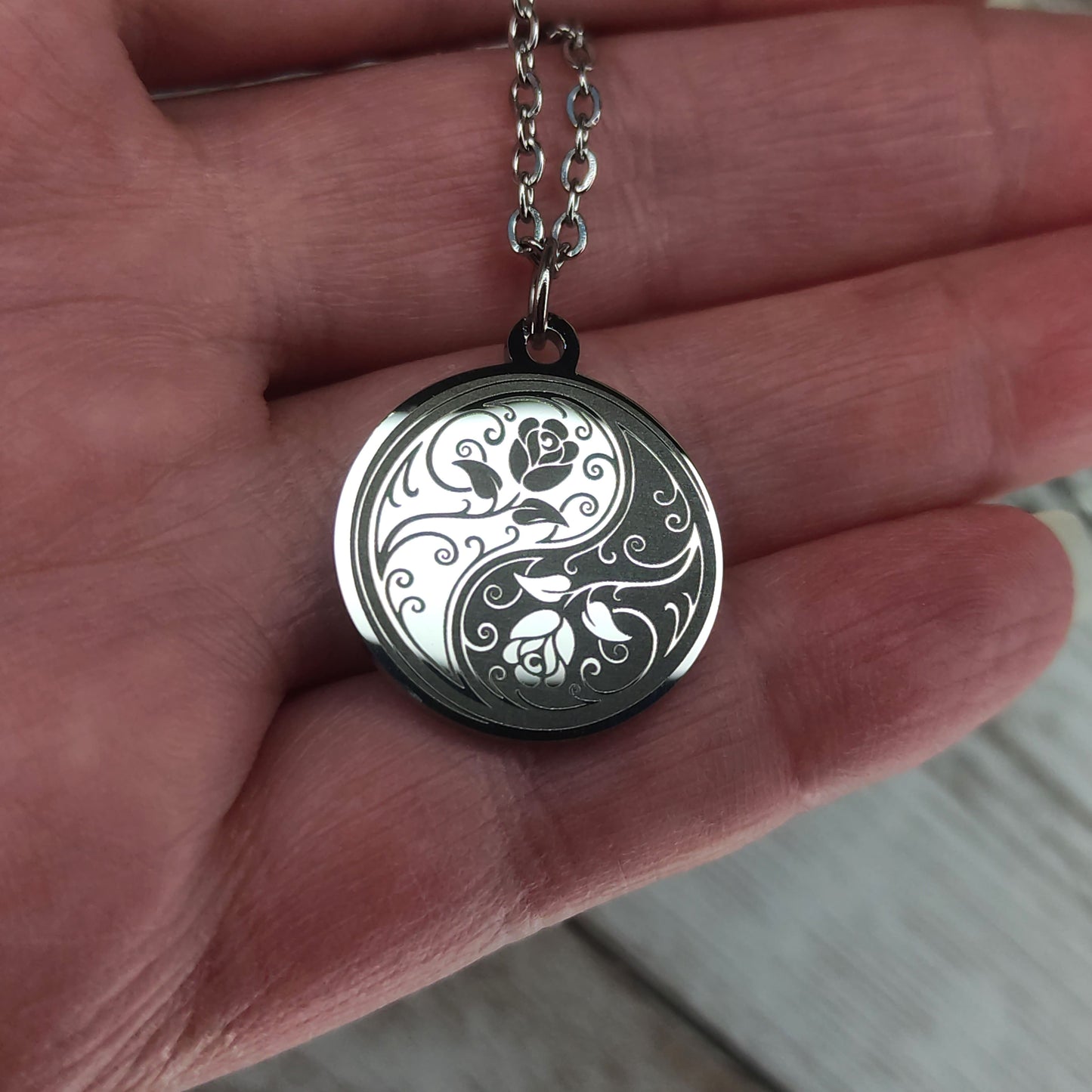 Collier médaille ronde en acier poli miroir avec gravure laser d'un symbole Yin Yang entrelacé de roses.