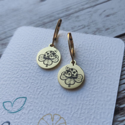 Paire de boucles d'oreilles dormeuses coccinelle acier inoxydable avec gravure laser trèfle sur médaillon poli miroir.