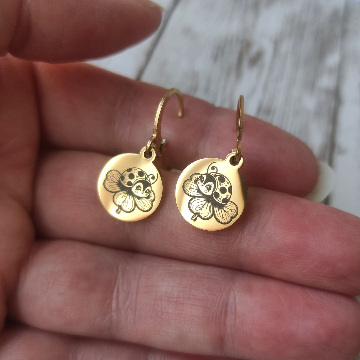 Paire de boucles d'oreilles dormeuses coccinelle acier inoxydable avec gravure laser trèfle sur médaillon poli miroir.