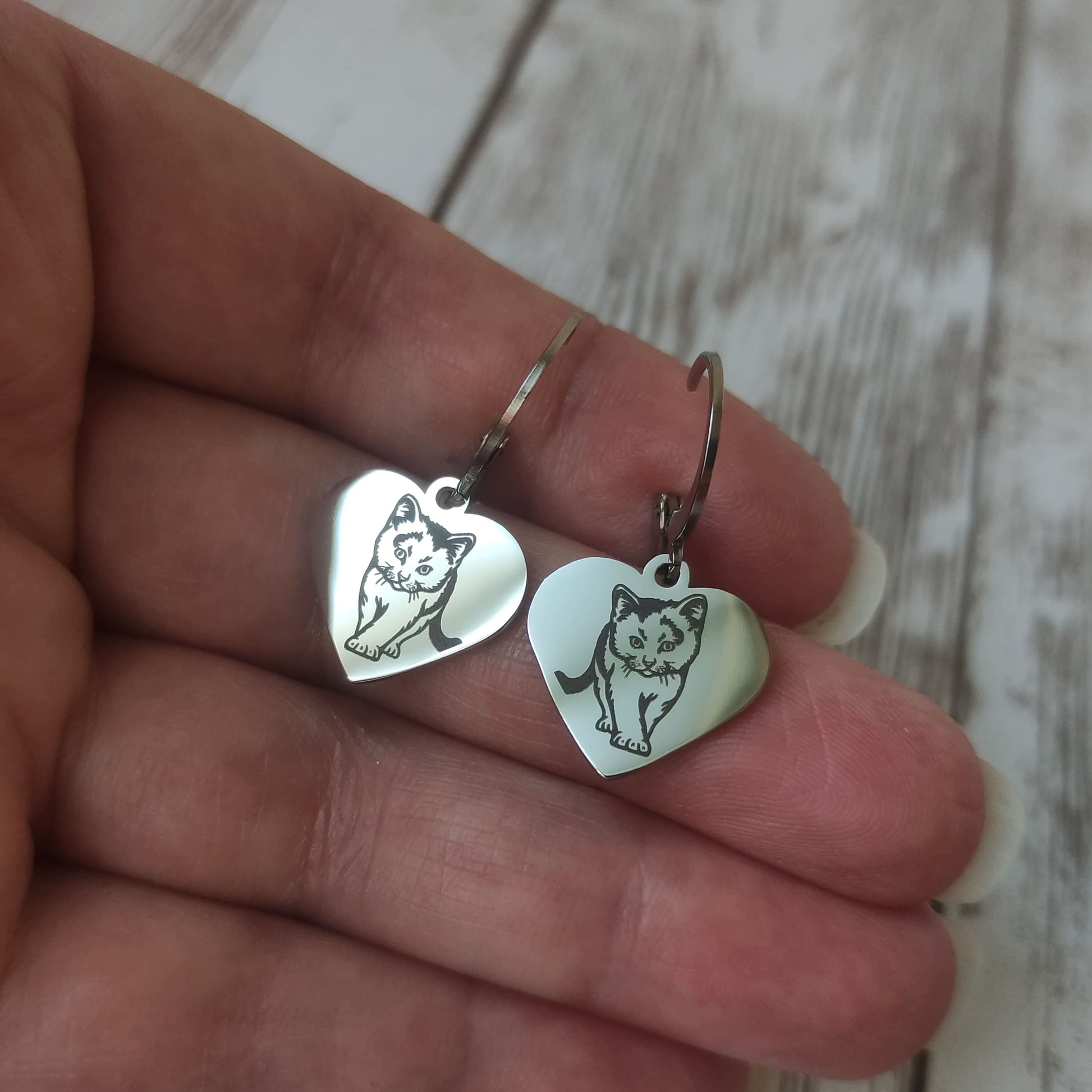Paire de boucles d'oreilles dormeuses en acier inoxydable avec pendentif coeur poli miroir et gravure laser d'un petit chat.