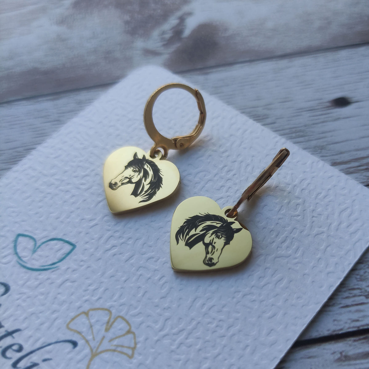 Paire de boucles d'oreilles dormeuses coeur cheval acier inoxydable avec gravure laser tête de cheval sur fond poli miroir.