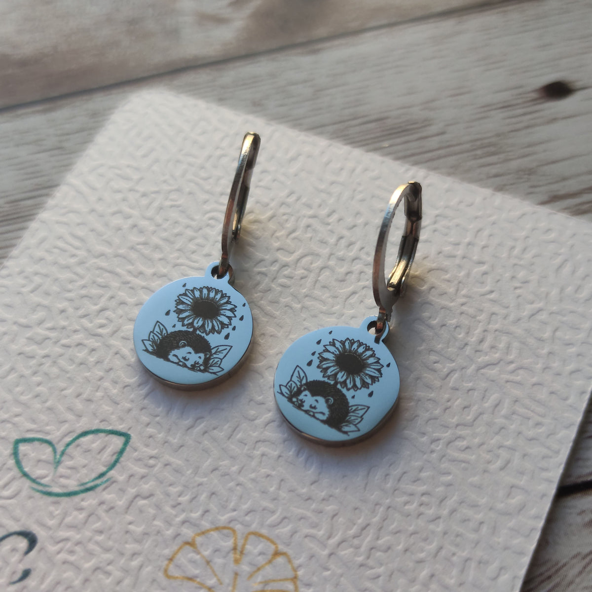 Boucles d'oreilles dormeuses en acier inoxydable poli miroir avec gravure laser d'un hérisson et d'un tournesol.