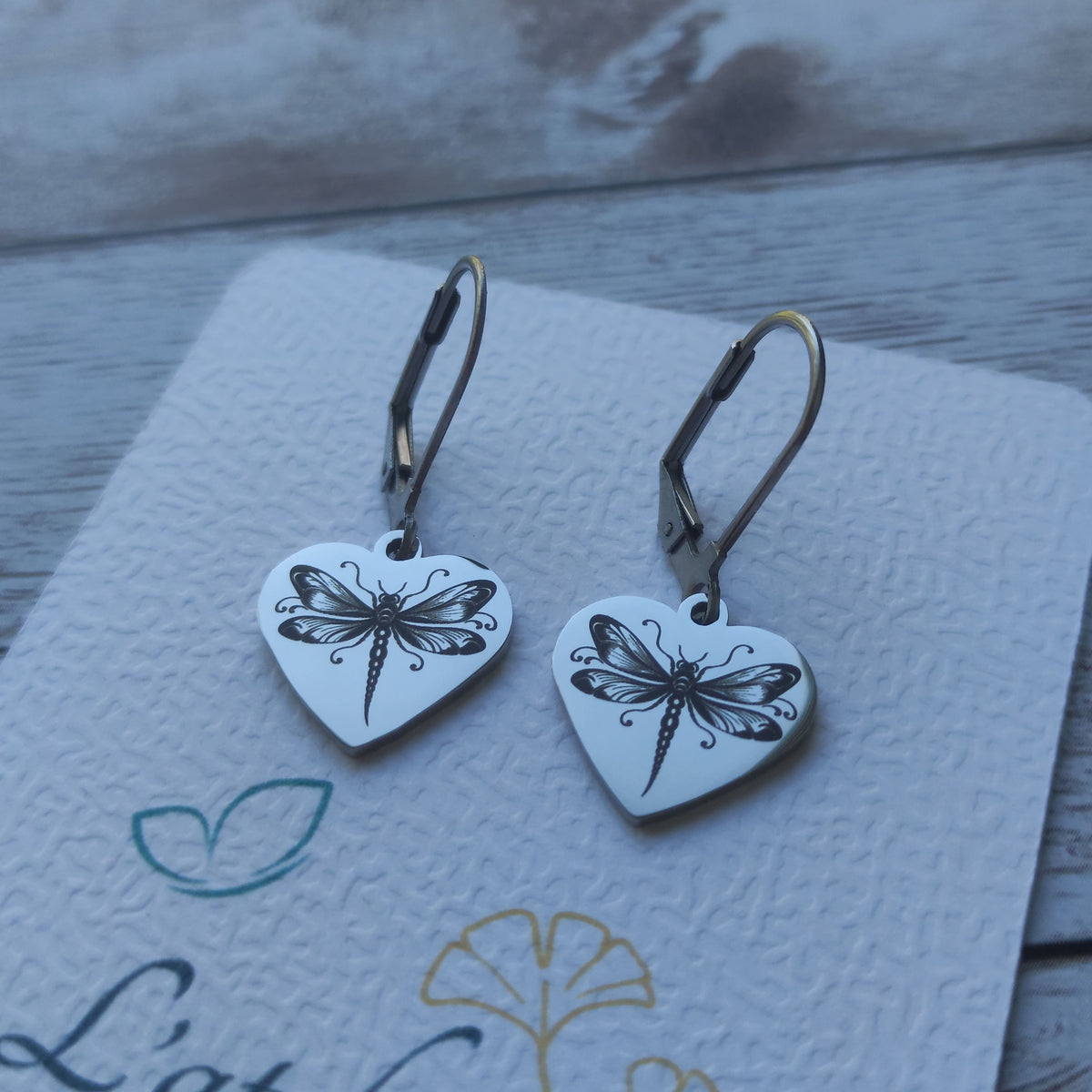 Paire de boucles d'oreilles dormeuses libellule en acier inoxydable avec pendentif cœur poli miroir et gravure laser de précision.