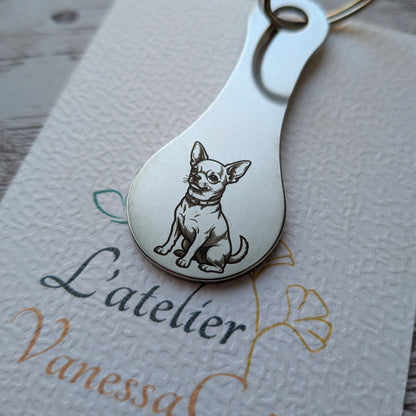 Porte-clés jeton de caddie en acier inoxydable gravé d'un petit chien de race Chihuahua assis, posé sur une carte de présentation de L'atelier Vanessa Créa.