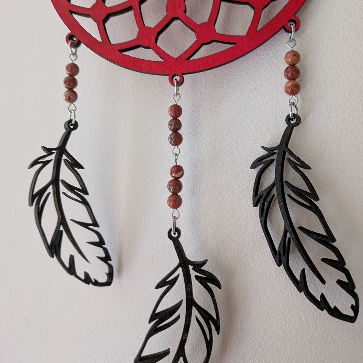 Zoom sur les plumes et perles en jaspe rouge de l'attrape-rêve