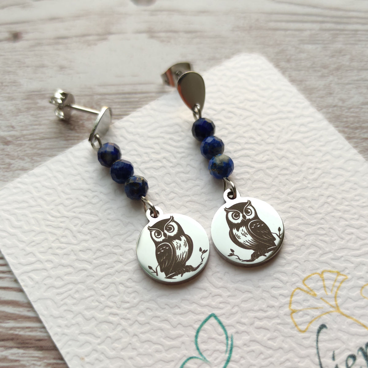Paire de boucles d'oreilles hibou en acier chirurgical et lapis-lazuli sur support de présentation.