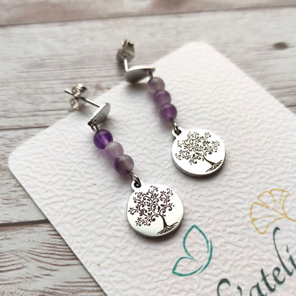 Paire de boucles d'oreilles pendantes avec motif Arbre de Vie gravé et perles d'améthyste sur carte de présentation L'atelier Vanessa Créa.