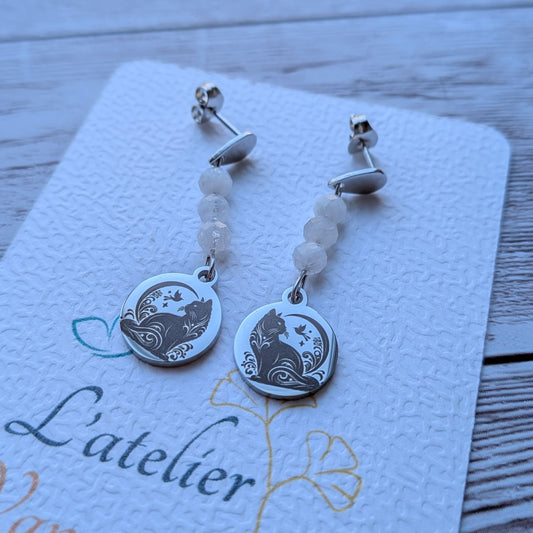 Paire de boucles d'oreilles pendantes avec motif chat gravé et perles naturelles sur carte de présentation L'atelier Vanessa Créa.