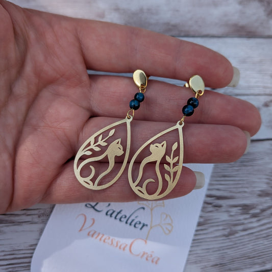 Boucles d'oreilles chat et feuillage ajouré en laiton avec perles d'œil de faucon de 4 mm, présentées sur la main avec la carte de l'atelier Vanessa Créa.