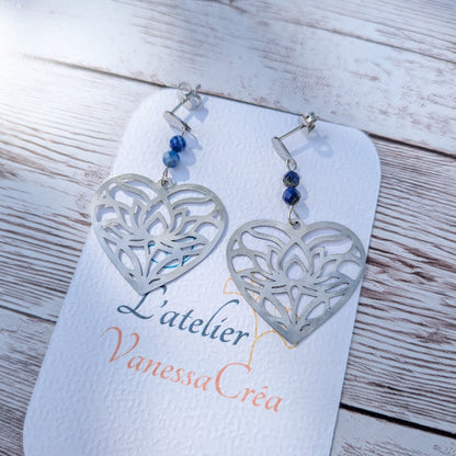Paire de boucles d'oreilles artisanales motif cœur ajouré en acier inoxydable et lapis-lazuli sur support de présentation.
