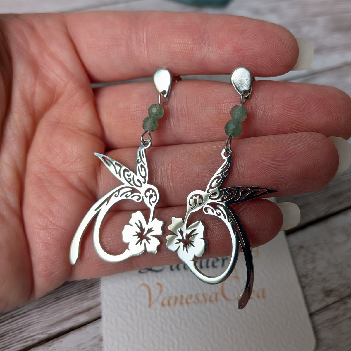 Paire de boucles d'oreilles colibri argentées en acier inoxydable tenue en main.