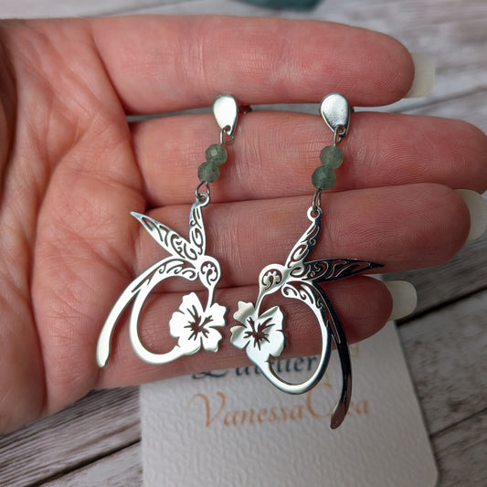 Paire de boucles d'oreilles colibri argentées en acier inoxydable tenue en main.