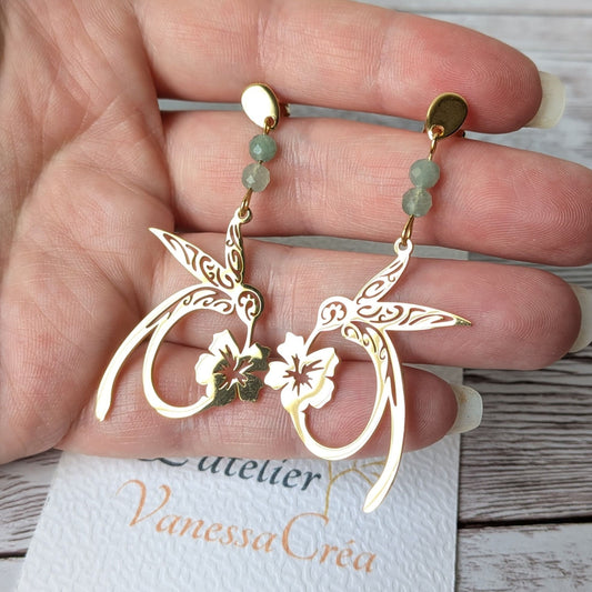 Paire de boucles d'oreilles colibri dorées en acier inoxydable tenue en main.