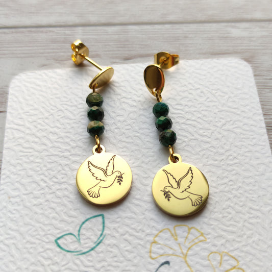 Paire de boucles d'oreilles pendantes dorées avec motif colombe gravé et perles de malachite sur carte de présentation L'atelier Vanessa Créa.