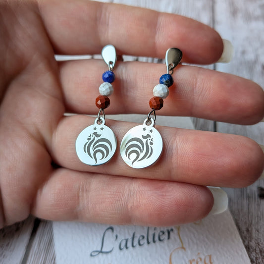 Boucles d'oreilles pendantes motif coq en acier inoxydable avec perles tricolores tenues dans la main.