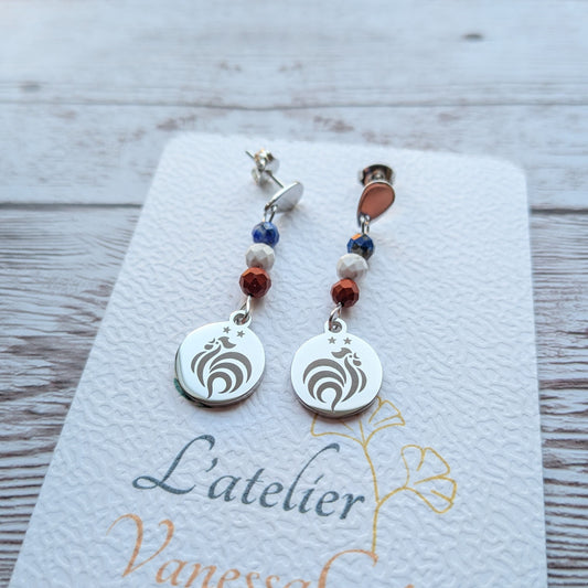 Paire de boucles d'oreilles pendantes avec motif coq gravé et perles de jaspe rouge, lapis lazuli et howlite sur carte de présentation L'atelier Vanessa Créa.