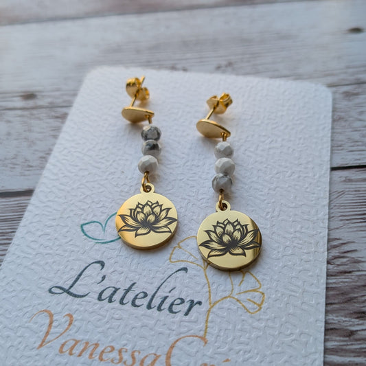 Gros plan de boucles d'oreilles pendantes dorées en acier inoxydable avec fleur de lotus gravée et perles de Howlite blanche sur carte de présentation "L'atelier Vanessa Créa"