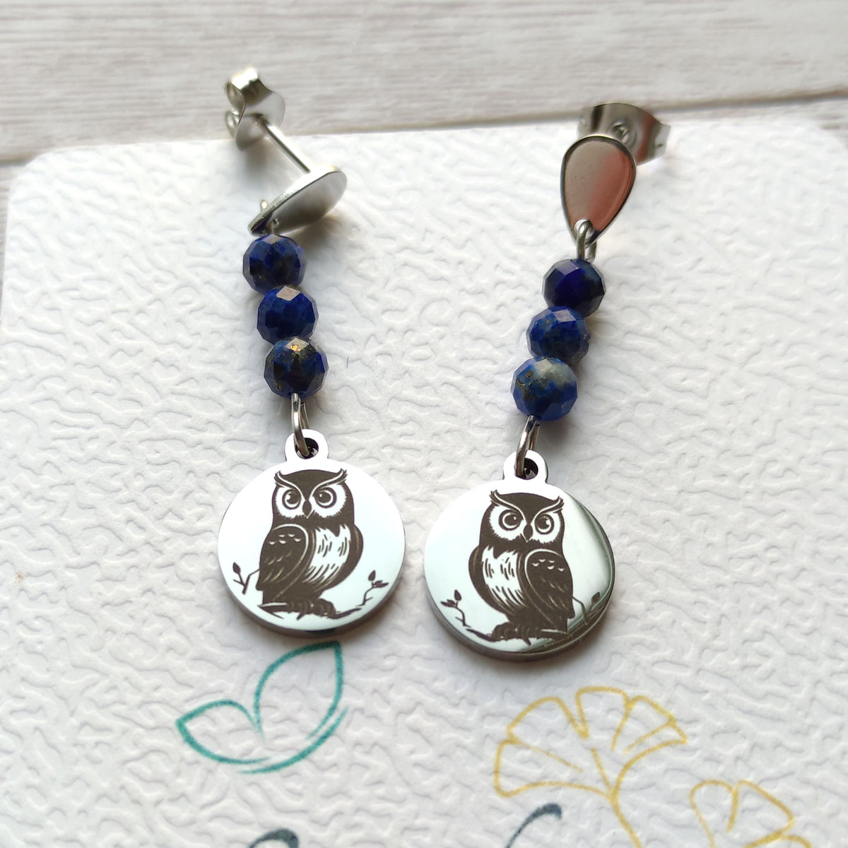Boucles d'oreilles pendantes hibou gravé en acier inoxydable avec perles de lapis-lazuli sur support Vanessa Créa.
