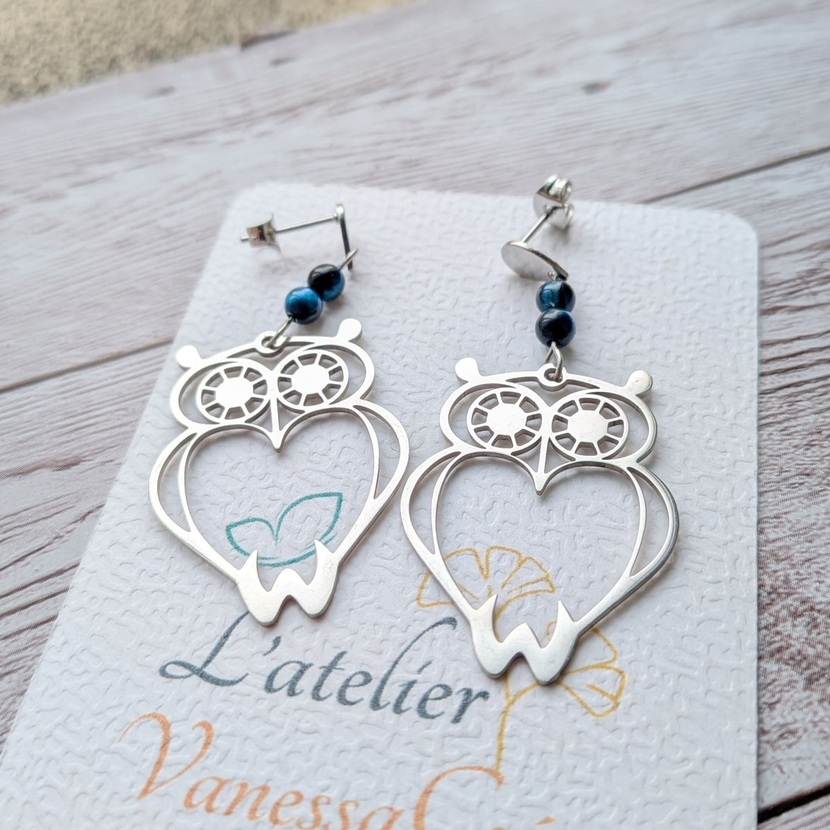 Vue détaillée de face des boucles d'oreilles hibou argenté et perles bleues.