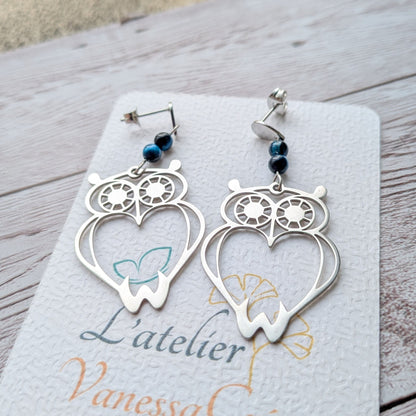 Vue détaillée de face des boucles d'oreilles hibou argenté et perles bleues.
