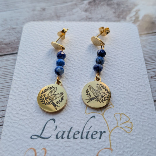 Paire de boucles d'oreilles pendantes dorées avec motif hirondelle gravé et perles de Lapis Lazuli sur carte de présentation L'atelier Vanessa Créa.