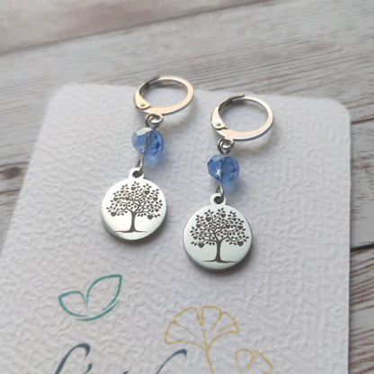 Boucles d'oreilles avec fermoir levier français, cristal à facettes bleu et médaillon rond en acier inoxydable gravé d'un arbre de vie avec cœurs.
