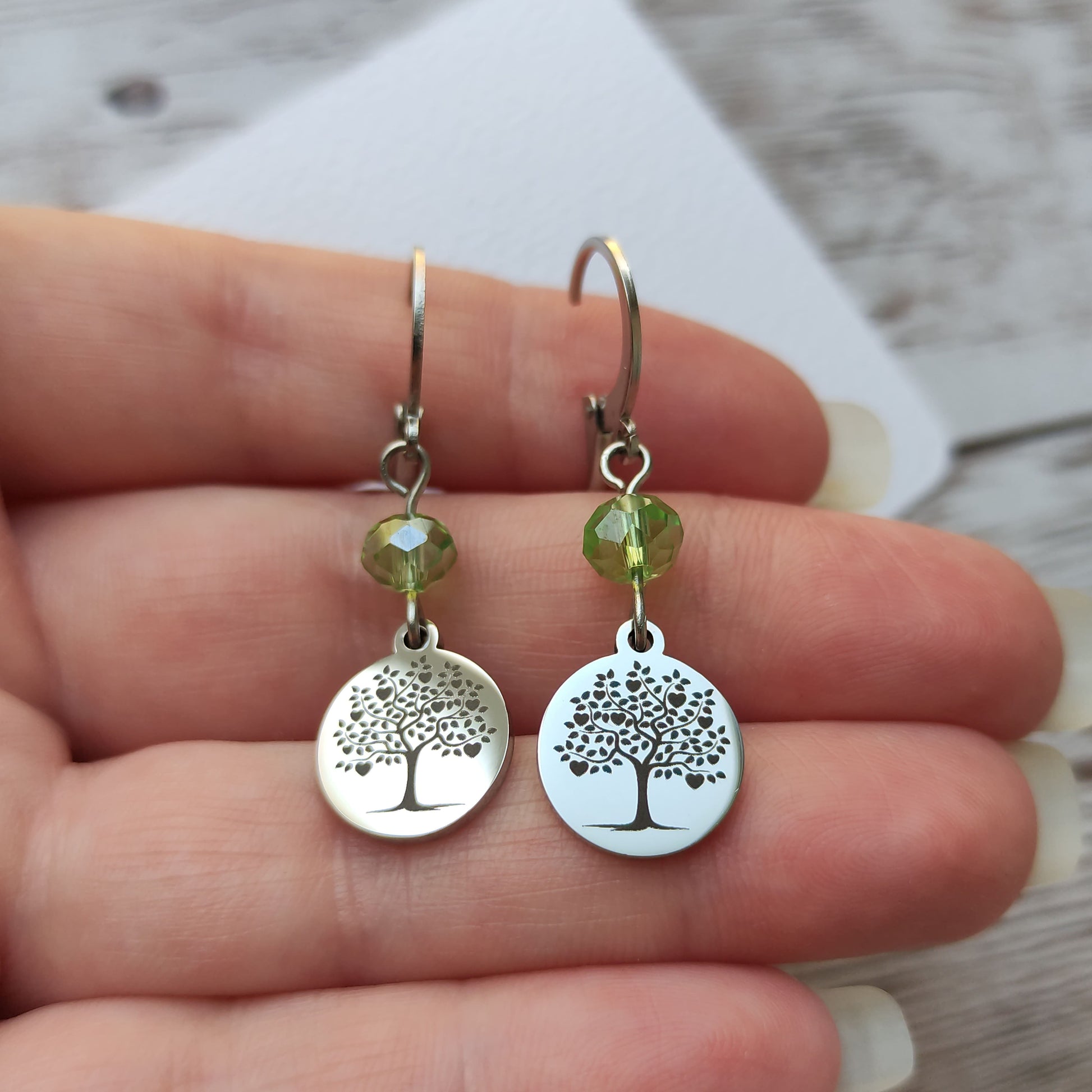 Boucles d'oreilles avec fermoir levier français, cristal à facettes vert et médaillon rond en acier inoxydable gravé d'un arbre de vie avec cœurs.