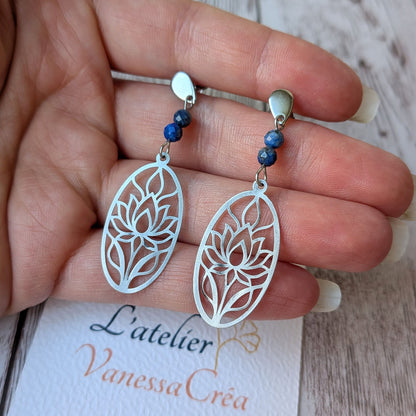 Boucles d'oreilles lotus ajouré en acier inoxydable et lapis-lazuli présentées sur la main avec la carte de l'atelier Vanessa Créa.