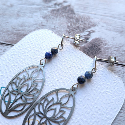 Paire de boucles d'oreilles lotus en acier inoxydable argenté et perles naturelles de lapis-lazuli sur support de présentation.