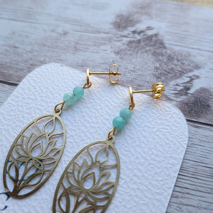 Paire de boucles d'oreilles artisanales motif lotus en laiton doré et perles d'amazonite naturelle posées sur support.