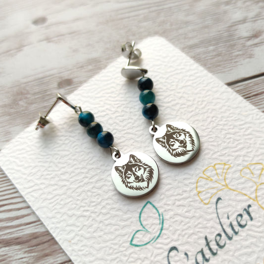 Paire de boucles d'oreilles pendantes avec motif loup gravé et perles d'œil de faucon sur carte de présentation L'atelier Vanessa Créa.