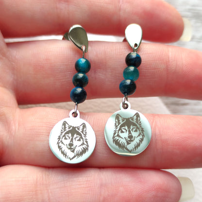 Boucles d'oreilles loup en acier inoxydable argenté tenues délicatement dans la main.