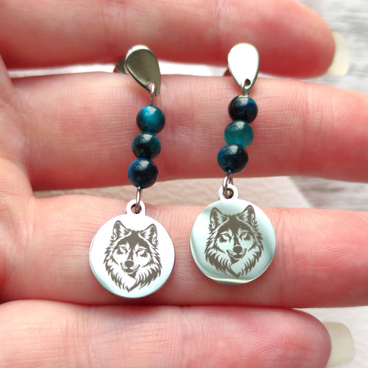 Boucles d'oreilles loup en acier inoxydable argenté tenues délicatement dans la main.